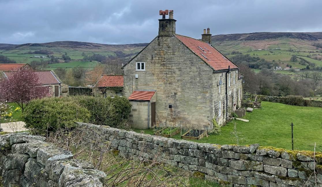 A stone house with a stone wall and grass
Description automatically generated